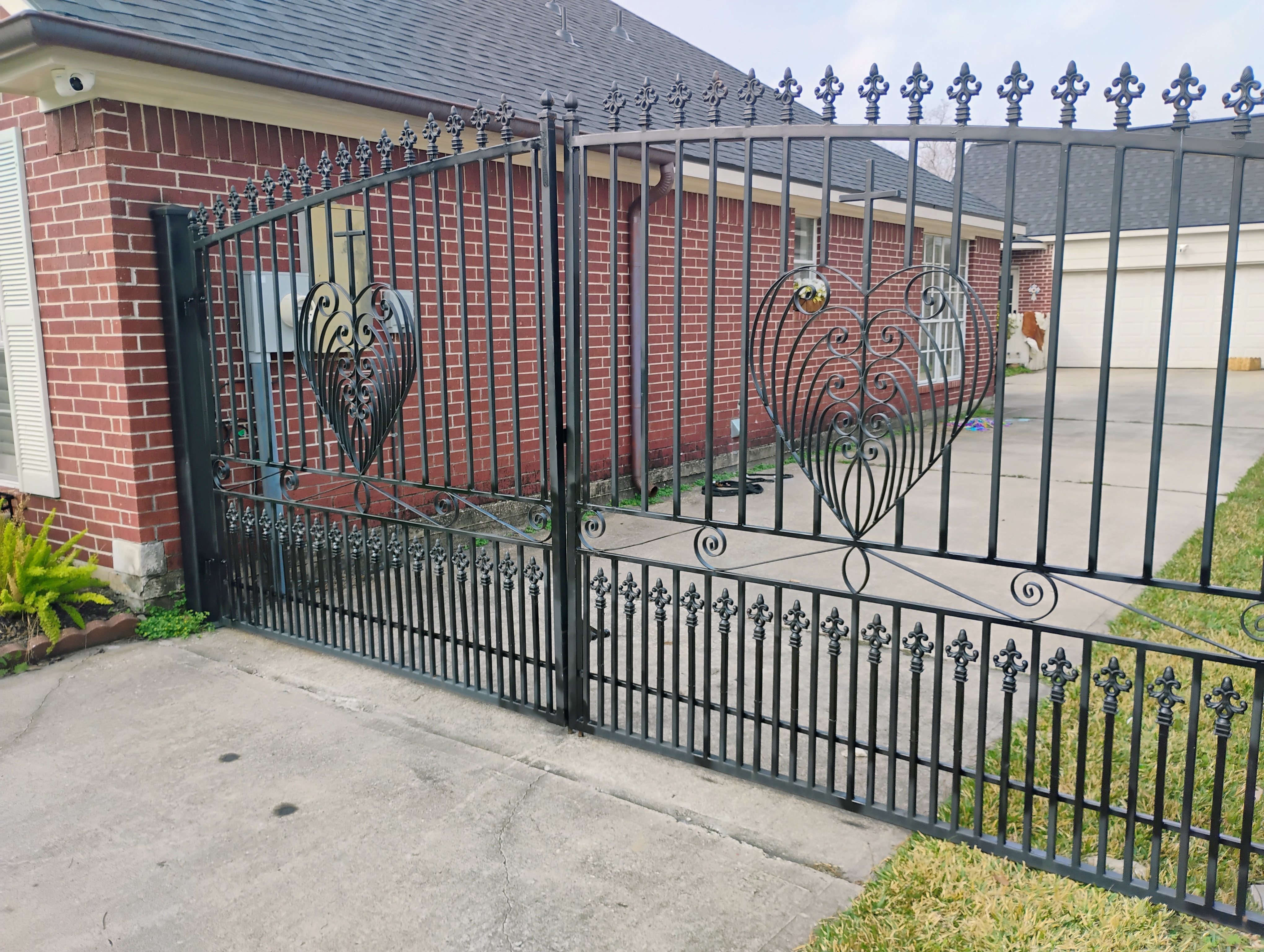 Angled view of custom black driveway gate featuring decorative heart scrollwork