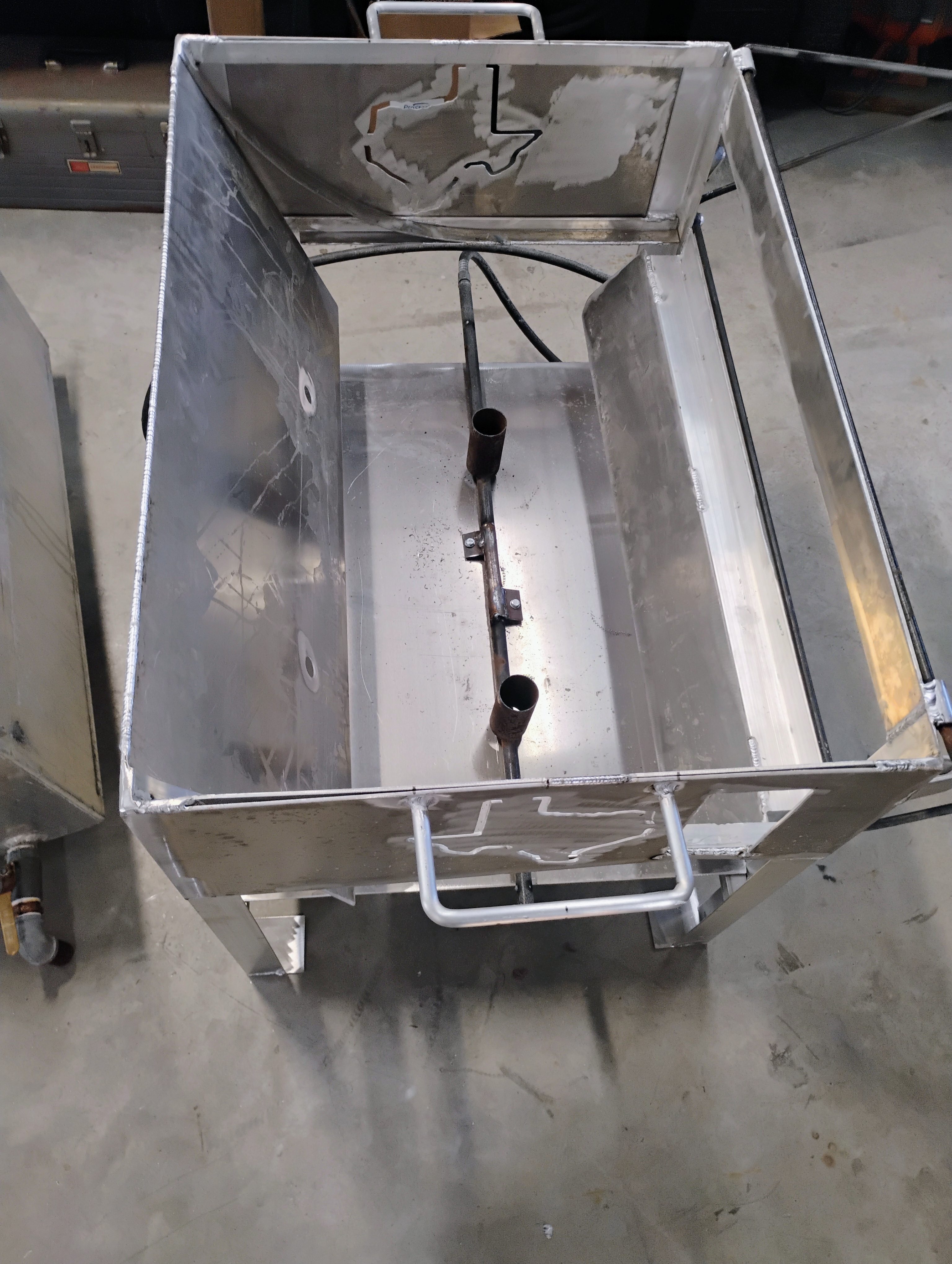 Top-down view of stainless cooker interior with burner tube layout